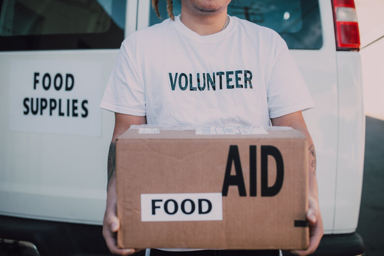 services-01 A volunteer holding a food aid box in front of a supply vehicle, ready for distribution.